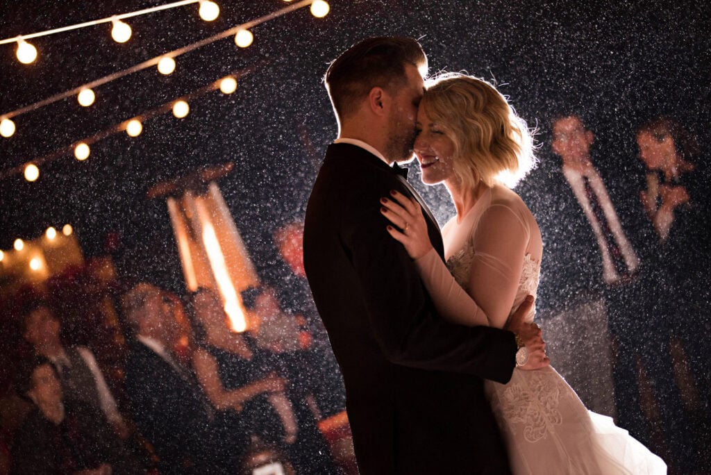 Couple dancing under string lights at night with rain or mist.