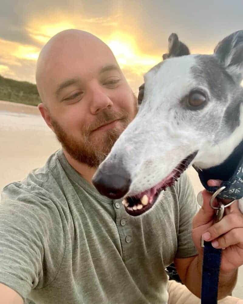 Man smiling with his dog during sunset on the beach.