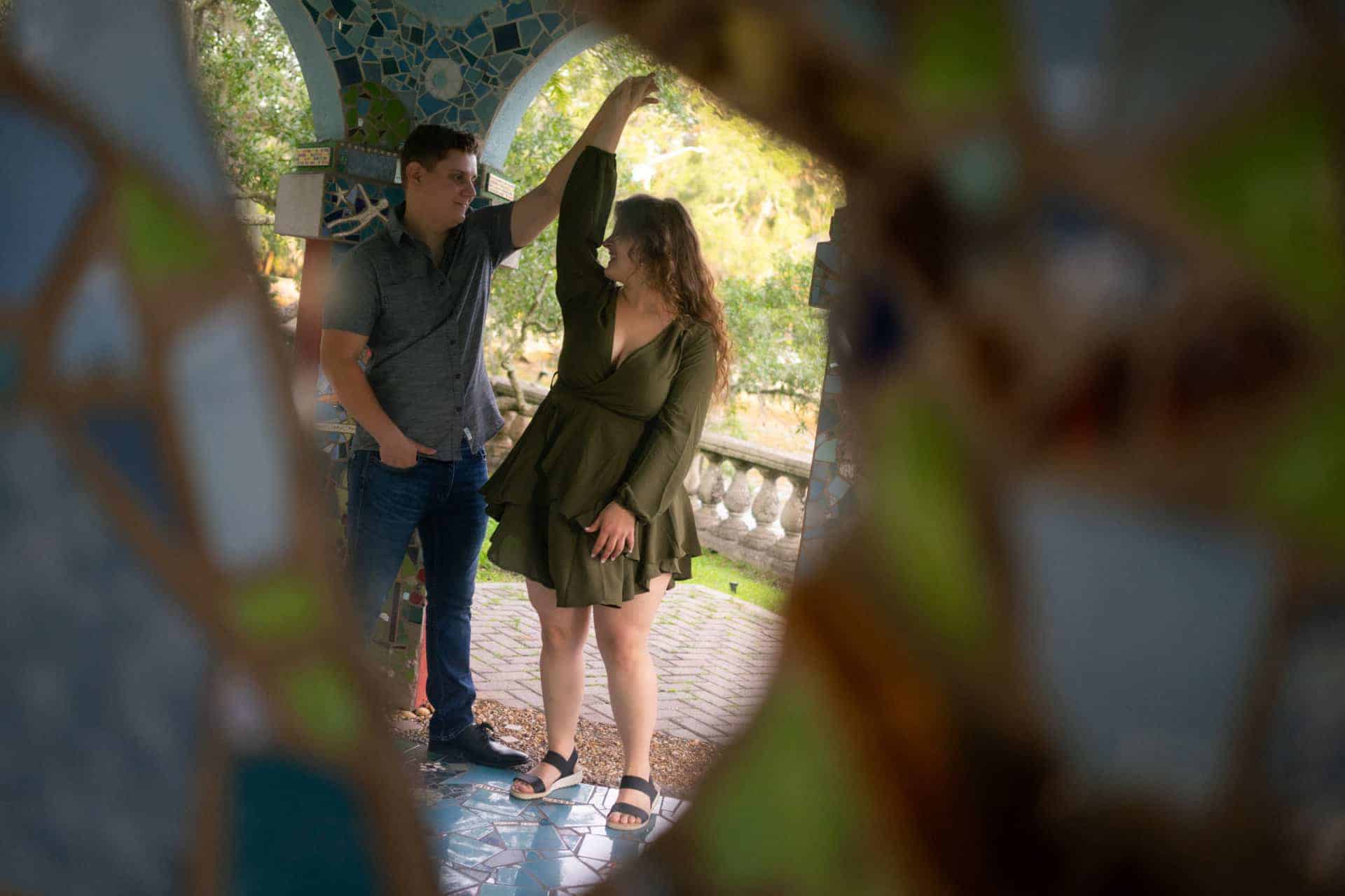 Romantic couple posing under a decorative archway in a park setting.
