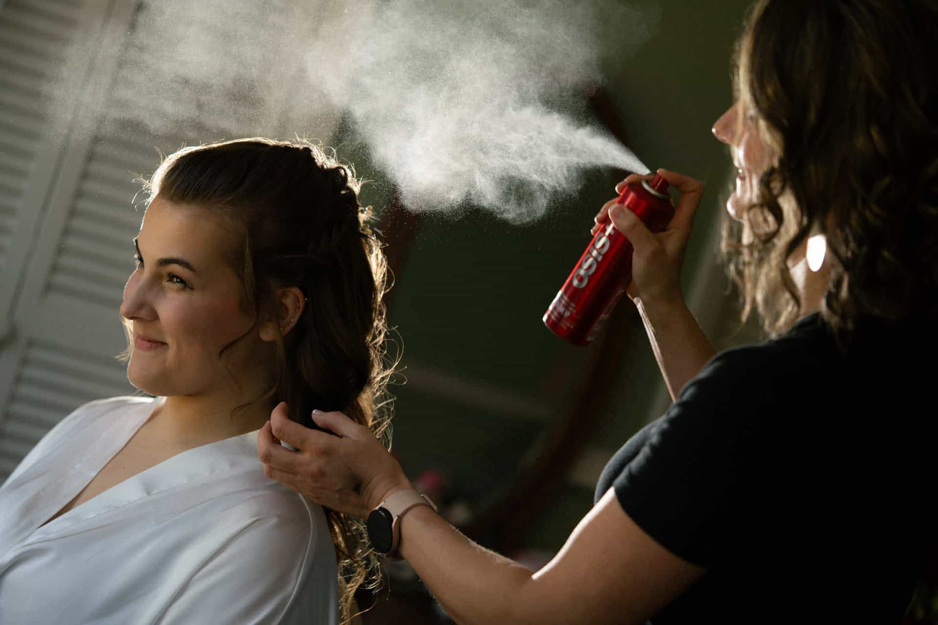 Bride getting her hair styled with spray in a professional photoshoot.