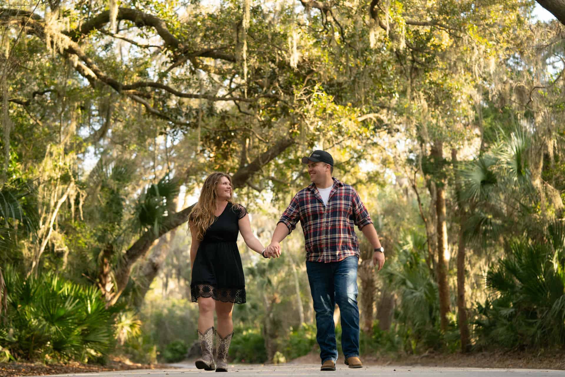 Couple holding hands walking through a lush forest in natural light.