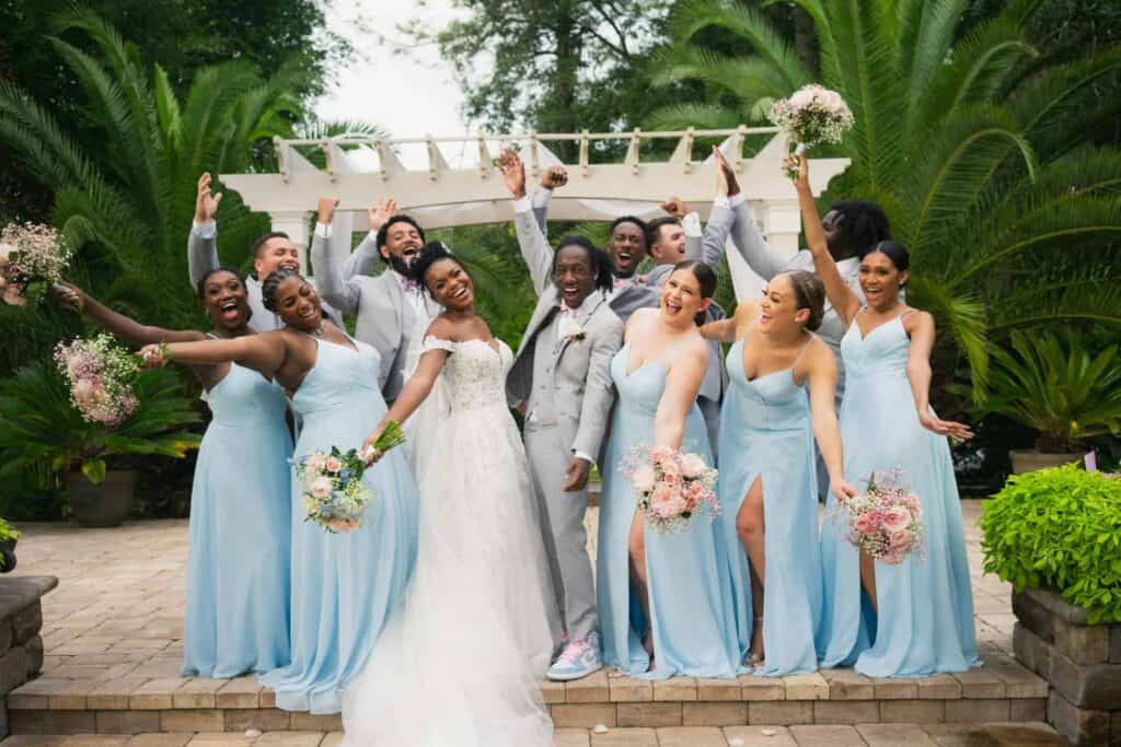 Joyful wedding party with bride, groom, and bridesmaids in a tropical garden.