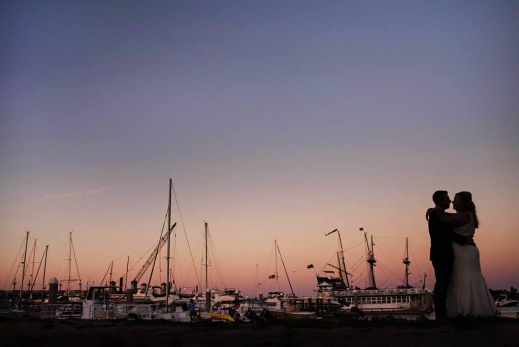 Silhouette of a couple embracing at sunset by the marina with boats.
