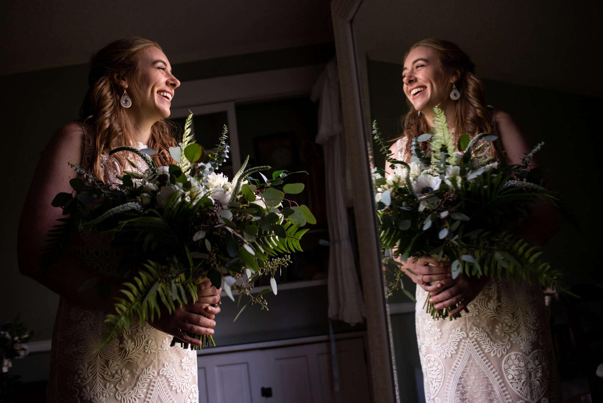 Bride holding a lush floral bouquet, smiling in front of a mirror.