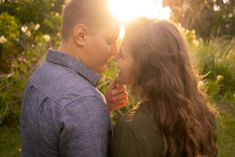 Man and woman lean in to kiss as the sun sets behind them