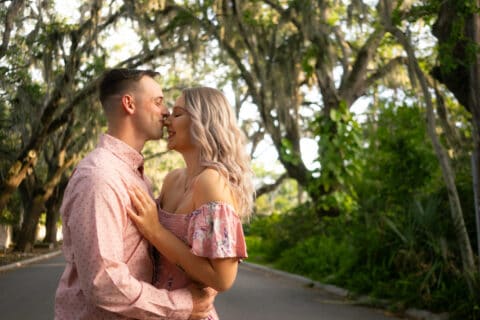 Man kisses a woman's nose on a street surrounded by greenery