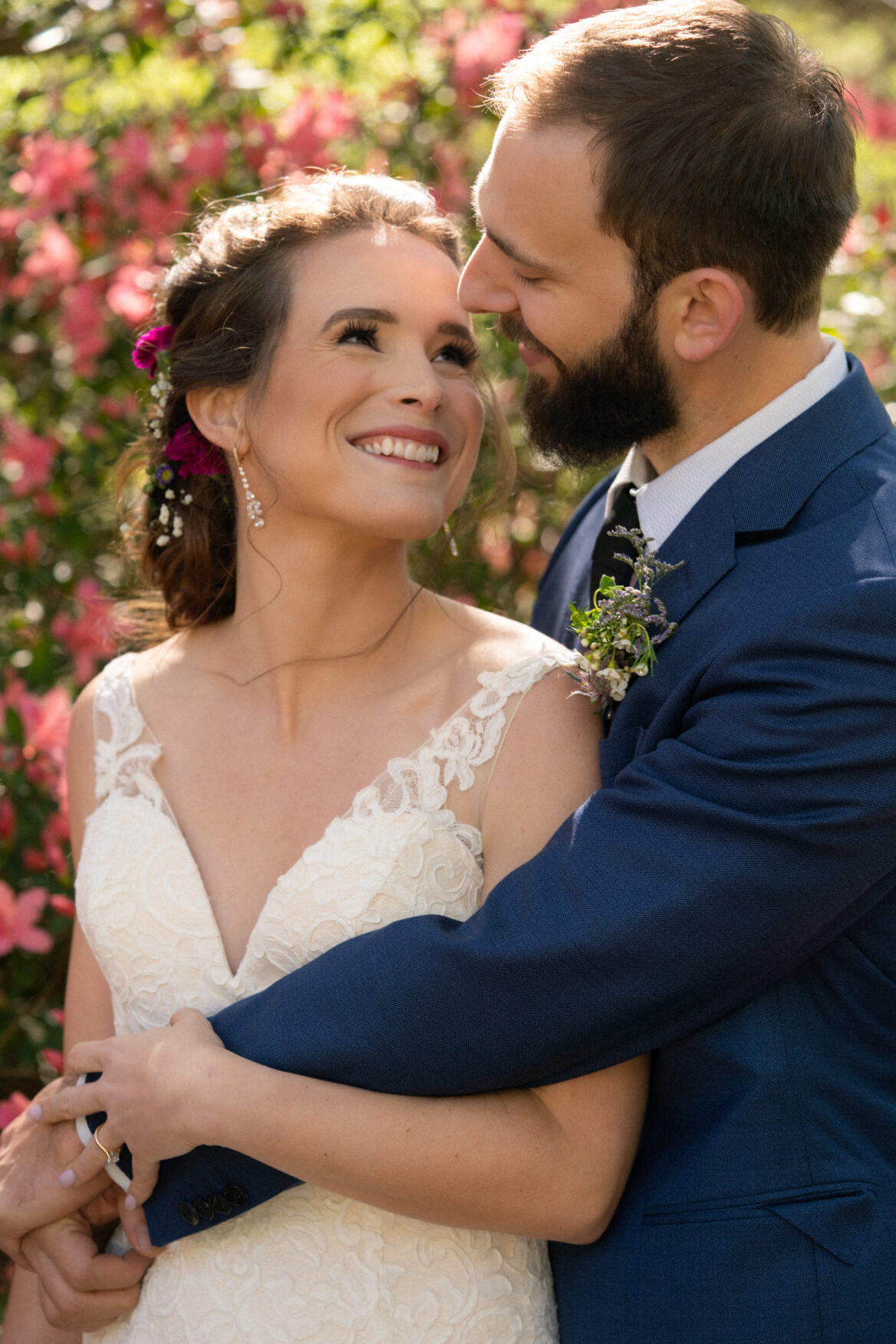 Bride and groom smiling at each other with flowers in the background