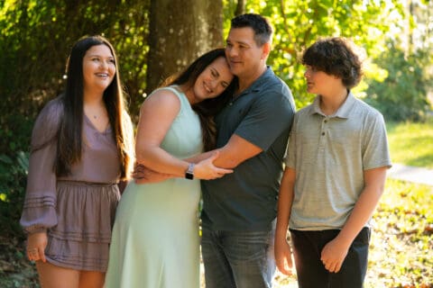 Family members smile and hold each other in front of greenery