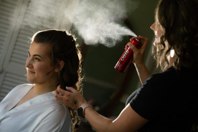 Hair stylist sprays hairspray on bride's hair