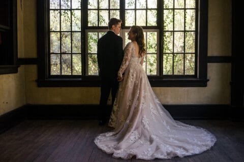 Bride and groom in front of large window with greenery outside