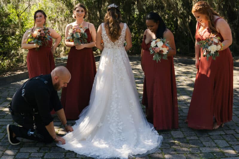 Wedding photographer helps a bride straighten her dress while bridesmaids watch