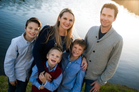 Family smiles and hold each other in front of a pond