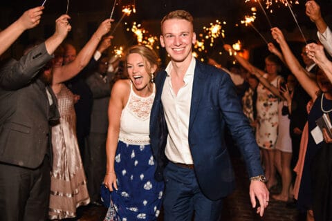 Bride and groom smile as wedding guests hold sparklers around them