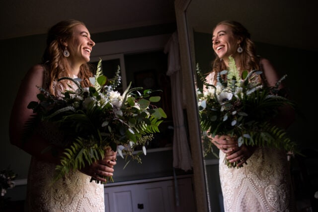 Happy bride smiles at her reflection in photo by wedding photographer chris david