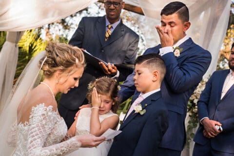 Bride reads to children while man cries during wedding