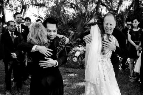 Black and white photo of bride and groom hugging their parents at wedding ceremony
