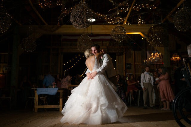 Bride and groom hold each other and dance with lights in the background