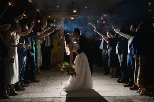 Bride and groom kiss while wedding guests hold sparklers around them