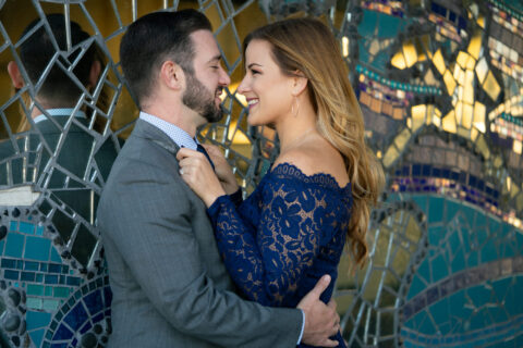 Man and woman hold each other in front of a glass mosaic wall