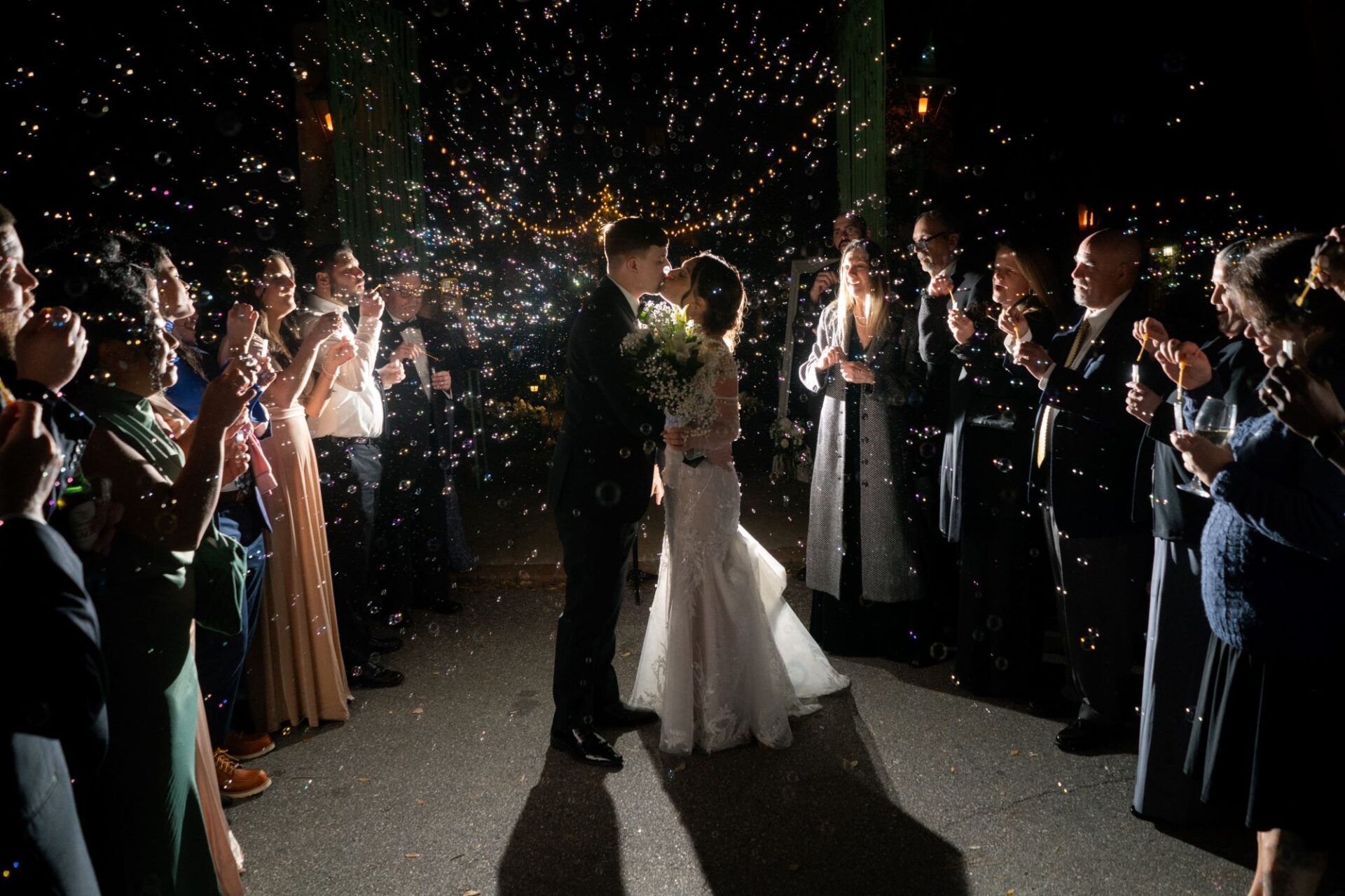 Bride and groom kiss while guests blow bubbles around them